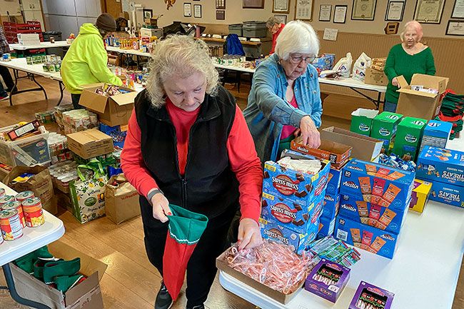 Starla Pointer/News-Register##At the McMinnville American Legion hall, Auxiliary members Susan Haley, Carol Doege and Glena Smith fill Christmas stockings with cards and snacks Tuesday for veterans in Yamhill County care homes. In the background, other auxiliary members set out cans and boxes of food this week so veterans and other people in need could “shop” for what they need over the holidays.