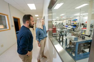 Rusty Rae/News-Register file photo##Applied Physics Technology office manager Kris Gullo and sales manager Eric Connors watch what’s going on in APT’s new state-of-the-art clean room, visible through large windows in the hallway.