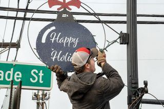 Rachel Thompson/News-Register##Firefighter Mitchell Melton removes one of the handmade ornaments from a pole on Trade Street Wednesday. The decorations will go into storage and be back again in by late 2024.