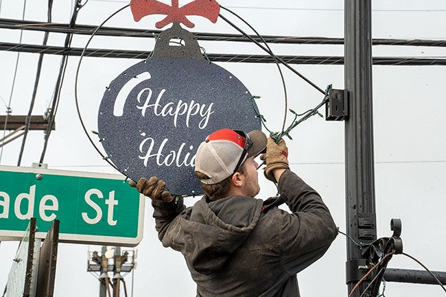 Rachel Thompson/News-Register##Firefighter Mitchell Melton removes one of the handmade ornaments from a pole on Trade Street Wednesday. The decorations will go into storage and be back again in by late 2024.