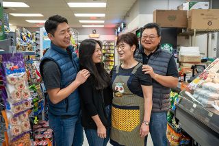 Rachel Thompson/News-Register##Jenny Kim, right, talks with her husband, Damon, and father Kenneth Kim, in back, in the family’s grocery and bento shop. As a child, Jenny played inside G&S Market, and now is learning more in order to be part of it. Staffing the counter is cashier Gabriel Ruiz Garcia.