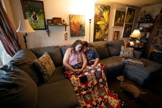 Rachel Thompson/News-Register##Laura and Doug Fugere comfort each other under a memorial quilt for their daughter, Shanny, who was killed in a crash caused by an intoxicated driver. On the wall are a photo of Shanny, her ashes in a wooden box, and art made by Doug of Shanny’s footprints, among other artifacts. Bean, at right, along with their dog Trip have also been a comfort to the Fugeres.