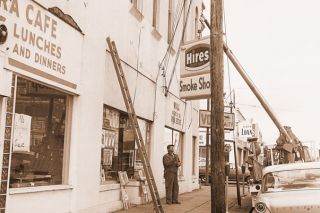 ##(March 1, 1969) Workmen take Smoke Shop sign down this week to make way for eventual building destruction. New tire store will replace four small businesses located in building at 3rd and Baker streets. Smoke Shop has long been a familiar landmark to townspeople and moved to its present location after a former building on 3rd Street also was destroyed four years ago. Mrs. Helen Collins, who runs the popular shop, is trying to find another location in the city. Other firms have moved to other locations, except one store owner who is retiring. [View is from the left side of Baker Street, looking north.]