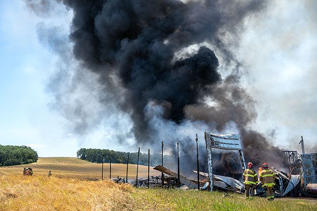 Rachel Thompson/News-Register##Hay barn fire smoke swirls in shades of black and gray as Jeff Nichols of Grand Ronde Fire District, and Daniel Cummins, of Sheridan Fire District, right, observe the blaze Tuesday. Fire officials were relieved the hayfield at left recently had been harvested, reducing risk of fire spreading to open ground.