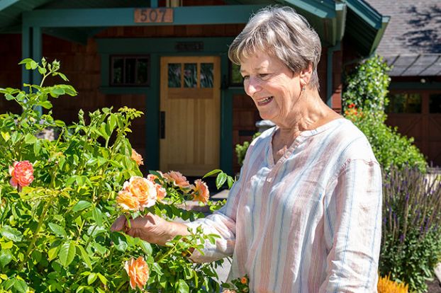 Rusty Rae/News-Register##Candace Van Zanten stops to smell the roses in front of her home at 507 N.E. 11th St., the McMinnville Garden Club’s Yard of the Month. She chose the yellow-orange “At Last” roses for their fragrance, as well as their beauty.