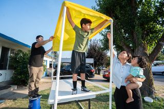 Rachel Thompson/News-Register##Landon Munoz holds up the yellow covering for the lemonade stand he and his brother, Max, are creating. Helping are their dad, Israel Sanchez, their mom, Maria Sanchez, and baby brother, Benjamin.