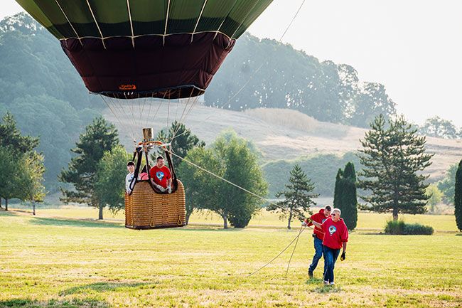 Rachel Thompson/News-Register##Siblings Austin Sherman, 14, and Priscilla Sherman, 11, of McMinnville, prepare for their first hot air balloon ride courtesy of pilot Eric Reid of Just in Kace in Albany at the Aug. 10 Rock of Ages Fun Festival. Tethering the balloon from the ground are Dubson Strickland, front, and Kyle Forslund. As they waved to mom Laura Sanchez, who was taking photos from below, she said, “Definitely the grumpiness of getting up this morning is gone.” After the flight, the kids agreed it was worth getting up early for.