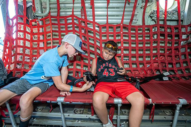 Rachel Thompson/News-Register##Lawrence Bennett, age 12, of Vancouver, helps Sammy Kelly, 8, of St. Helens figure out how to buckle the seat belt in a C-130 Hercules aircraft, while waiting in line to see the cockpit. Lawrence’s grandfather is a pilot and he likes military planes; Sammy loves planes and helicopters, and has with him a model of his favorite plane, an F-14.