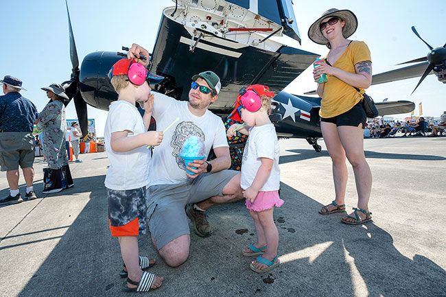 Rachel Thompson/News-Register##Taking a snow-cone break in the shade of a plane wing are Matthew and Christina VanCleave of Tigard and their children, Daxton, 4, and Quinley, 2, whose ears are also well-protected for the occasion.