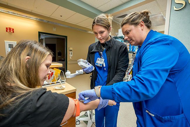 Rachel Thompson/News-Register##New registered nurse Grace Umfleet, center, and her preceptor, Emily Lambert, RN, practice using a scanner to find a patient’s veins. Ashley Garrett, one of Willamette Valley Medical Center’s educators, is standing in as the patient during a practice session for Umfleet’s nurse residency program. A month after graduating from George Fox University in June, Umfleet started the program, designed to give newly graduated nurses extra training and help them settle into their work at WVMC.