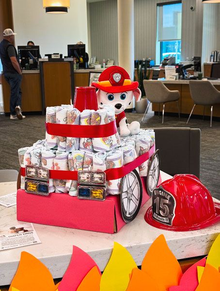 Rusty Rae/News-Register##“Sparky the Fire Dog” rides a stack of diapers shaped like a fire engine in the downtown McMinnville First Federal lobby. It’s part of a competition among the company’s branches to help boost the diaper drive benefiting A Family Place.