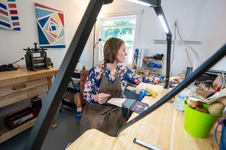 Rachel Thompson/News-Register##Framed by a moveable arm that keeps power tools within easy reach, jewelry artist Amber Joy Dutchuk selects pieces for her latest project. She created the workshop at her McMinnville home, adding a desk that’s just the right height for her work.