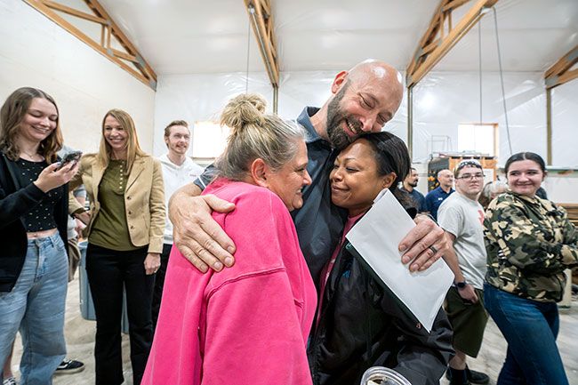 Rachel Thompson/News-Register##CTE teacher John Stearns, who won the Harbor Freight award, hugs colleagues Jill Whitehead, left, and Tashi Haarsma at the surprise event Tuesday. In the background on left are his daughter, Riley; wife, Katie; and son Bryce; son Brian also was there and other sons Derryk and Dylan congratulated him on Facetime. Students at the event included Kaylee Robinson, right.