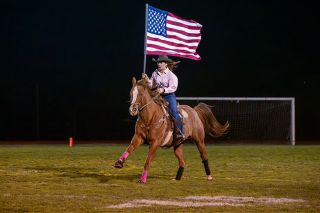 Rusty Rae/News-Register##Lady, a 21-year-old appaloosa, and her owner Sophia Crawford, carry the U.S. flag across the Yamhill Carlton High School football field Friday, Oct. 25, during the National Anthem ceremony. It was the final game for Lady, who is retiring.