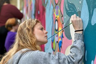 Kirby Neumann-Rea/News-Register##Linfield student Bailee Romine adds fine detail to the “mushroom lady” element on the mural “Roots of the Heart” at the Miller Art Center. Romine considers the mural a visual “trip” open to interpretation.