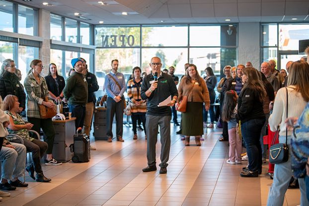 Rusty Rae/News-Register##Beto Reyes, one of the Chamber ambassadors, emcees the Oct. 25 Greeters event in the showroom at Lum’s GMC. About 80 people form a circle to share information about their companies and organizations from 8 to 9 a.m.