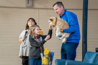 Rachel Thompson/News-Register##Yamhill-Carlton Elementary School third-grader Lillian Powers pets Gobi, the star of the “Finding Gobi” books, held by her owner and best friend, author Dion Leonard. YCES Librarian Kristin Pond is in the background. Gobi is wearing a collar handmade by Lillian in the school colors, black and orange. She wrote to Gobi and Leonard, asking them to visit her school.