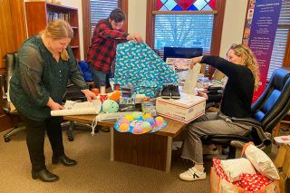 Starla Pointer/News-Register##CASA director Sarah Johnson, left, volunteer coordinator Sebastian Fisher and case manager Ellie Vityukov rush to wrap last-minute gifts for children, in time for the gathering on Dec. 19 when CASA advocates picked up the wrapped gifts for delivery. The staff members said they also had a chance to enjoy delivering a few.