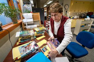 Rachel Thompson/News-Register##Judie Folgate, whose volunteer job with the Friends of the Library is overseeing the memorial and celebration book program, checks on new volumes purchased with donations in honor of local residents. Folgate also oversaw the program when she worked at the library before retiring in 2006.