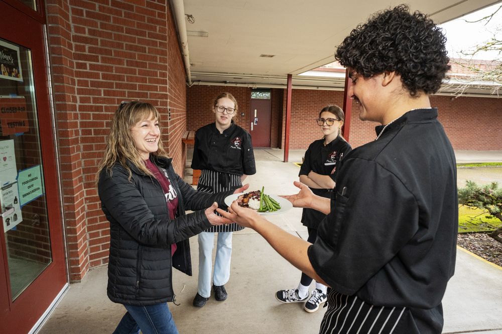 Rachel Thompson/News-Register##Dayton High librarian Melissa Oliveira accepts a plate from ProStart team member Erick Chinchilla. In the background are fellow team member Grace Goularte, and team manager Abbigale Rowles.