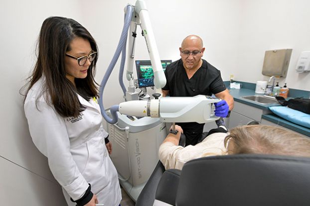 Rusty Rae/News-Register##Dermatologist Dr. Stephanie Campbell and radiation tech Mike Hurtado prepare to scan an area on pretend patient Starla Pointer’s forearm as they demonstrate one of their diagnostic tools. The machine also is used in treating skin cancers.