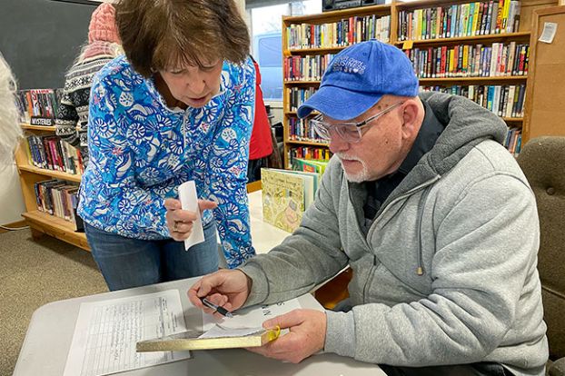 Starla Pointer/News-Register##Library volunteers Diana White, left, and Bill Lucas review paperwork as White signs up for her library card.