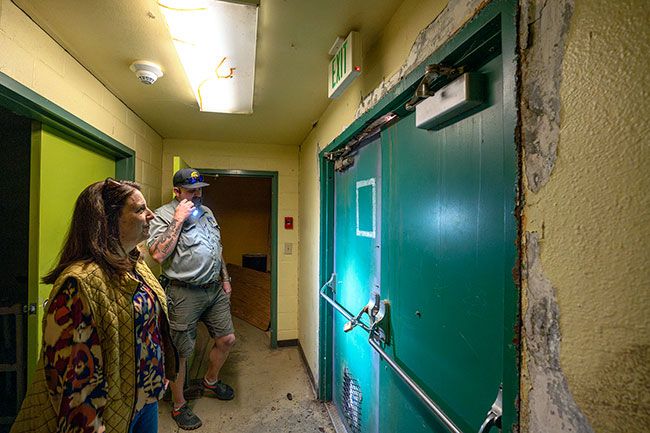 Rachel Thompson/News-Register## Superintendent Dorie Vickery and Operations and Facilities Manager Sean Vesper inspect a back door to the locker rooms and storage area of the old gym at Faulconer-Chapman School. The lime cement has eaten away at the steel door, which staff has chained shut to prevent trespassing. A grate has been welded to the bottom of the door to provide air flow to the damp, humid space.