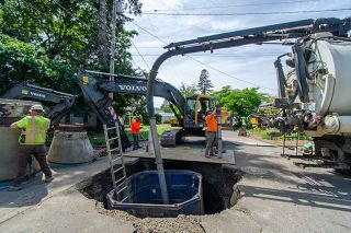 Rachel Thompson/News-Register##Workers replace a leaking manhole at the intersection of Southeast Storey and Rummel streets in McMinnville on Wednesday as part of an ongoing city sewer project. A shoring box is used to protect workers in the ground as an excavator prepares to lift the manhole. Rachel Thompson/News-Register##Workers replace a leaking manhole at the intersection of Southeast Storey and Rummel streets in McMinnville on Wednesday as part of an ongoing city sewer project. A shoring box is used to protect workers in the ground as an excavator prepares to lift the manhole.