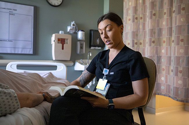 Rachel Thompson/News-Register##Andrea McCracken, a respiratory therapist at Willamette Valley Medical Center, reads to a simulated patient, played by nurse Melissa Faubion, in her role as a volunteer for the No One Dies Alone program. McCracken was one of the first volunteers to sign up and help ensure no one is forgotten in their final hours. Rachel Thompson/News-Register##Andrea McCracken, a respiratory therapist at Willamette Valley Medical Center, reads to a simulated patient, played by nurse Melissa Faubion, in her role as a volunteer for the No One Dies Alone program. McCracken was one of the first volunteers to sign up and help ensure no one is forgotten in their final hours.