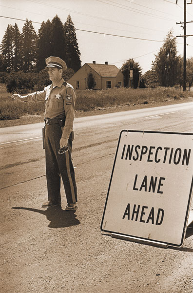(July 1, 1970) Sgt. Al Cianni, who used to be stationed at the local state police office, directs vehicles into spot safety check area on Highway 99W near Dundee last week. Two signs were put up telling drivers to slow up. Not all cars were directed into inspection area, in fact many turned in without being directed. Most common deficiency found was light problems, particularly signal lights. (July 1, 1970) Sgt. Al Cianni, who used to be stationed at the local state police office, directs vehicles into spot safety check area on Highway 99W near Dundee last week. Two signs were put up telling drivers to slow up. Not all cars were directed into inspection area, in fact many turned in without being directed. Most common deficiency found was light problems, particularly signal lights.