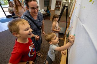 Rachel Thompson/News-Register##Nolan Ewing, 7, smiles as his brother Colton, 4, places a square on the community paint-by-sticker masterpiece with help from their mom, Jennifer, at the McMinnville Community Center on Thursday. Rachel Thompson/News-Register##Nolan Ewing, 7, smiles as his brother Colton, 4, places a square on the community paint-by-sticker masterpiece with help from their mom, Jennifer, at the McMinnville Community Center on Thursday.