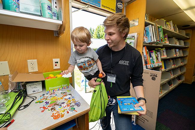 Rachel Thompson/News-Register##Bennett Look, 2, reaches for a sticker inside the library bookmobile after checking out books with his dad, Dayton, during Wednesday’s Read & Play program at Joel Perkins Park in Lafayette. Rachel Thompson/News-Register##Bennett Look, 2, reaches for a sticker inside the library bookmobile after checking out books with his dad, Dayton, during Wednesday’s Read & Play program at Joel Perkins Park in Lafayette.