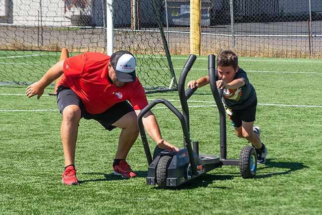Nathan Ecker/The News-Register##Matson switches the intensity on the magnetic weight sled for Blake Littlewolf who wanted more weight. The sled easily allows someone to switch between lighter and heavier weight, allowing more flexibility in the workout process and quicker transitions for varying age groups who have different strengths. This activity involved every child in a team-like event where participants pushed the sled back and forth in a ten-yard margin and cheered each other on.