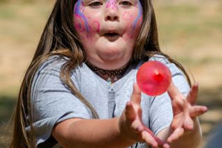 Rachel Thompson/News-Register##Seven-year-old Ella Newcomb of Amity reaches to catch a flying water balloon during a toss game at Amity Day.