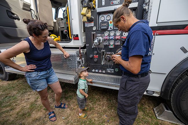 Rachel Thompson/News-Register##Carlton Firefighter EMT Jenny Wilson chats with 2-year-old Ryland Fox while showing him around the firetruck during the Tuesday event. Ryland, with his mom Rachel at left, has been fascinated by fire engines since seeing them in the Carlton Fun Days parade earlier this year.