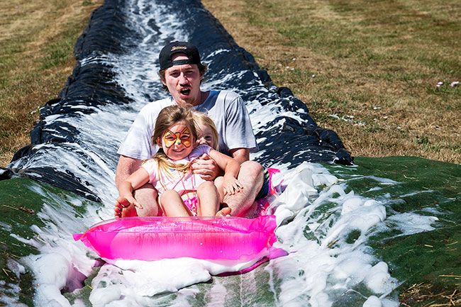 Rusty Rae/News-Register##Jared Ulan of McMinnville holds on to daughters, Paisley and Paityn, as they roll down the slip and slide at Rock of Ages Fun Festival on Saturday, Aug. 9. Kids also had a bounce house, a candy bomber, carriage rides and more to keep them entertained throughout the day.