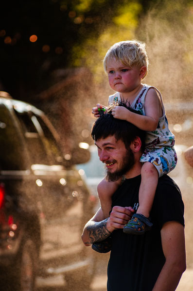Rachel Thompson/News-Register##Two-year-old Oliver Cartwright of Aurora, clutching a toy car, watches real ones go by from atop dad Christian’s shoulders as they enjoy a cooling mist on Third Street. Rachel Thompson/News-Register##Two-year-old Oliver Cartwright of Aurora, clutching a toy car, watches real ones go by from atop dad Christian’s shoulders as they enjoy a cooling mist on Third Street.