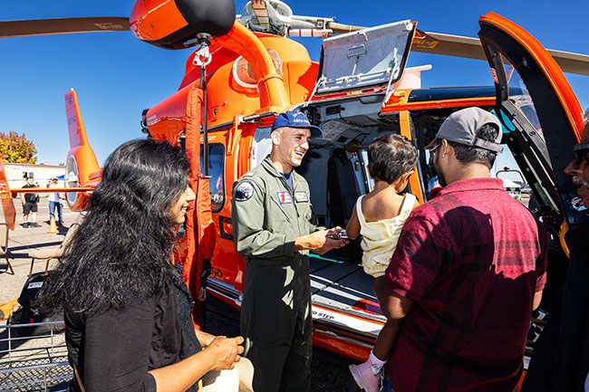 Rachel Thompson/News-Register##Lt. Dan Fiorvanti of the U.S. Coast Guard offers a peek inside a rescue helicopter to 2-year-old Nadini Samarakoon of Hillsboro, held by her father, Anjana Samarakoon, as her mother, Udari Jayasiri, looks on. The North Bend-based crew was among several giving tours as air show attendees explored a wide range of aircraft and chatted with those who fly and maintain them.