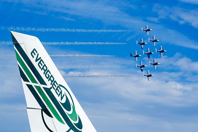 Rachel Thompson/News-Register##The Canadian Forces Snowbirds soar beyond the tail of an Evergreen 747 on Saturday. The nine-jet aerobatic team performed above McMinnville Municipal Airport, while spectators gathered across the street on the lawn of the Evergreen Aviation & Space Museum, and along nearby roads to watch the precision-flying spectacle.