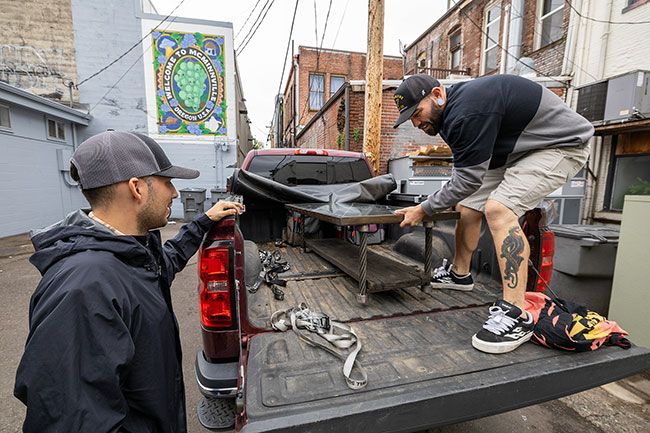 Rachel Thompson/News-Register file photo##Recology Waste Zero Specialist Kade Klienstuber, left, helps artist-in-residence Blaine Niehus unload a recycled-material coffee table in October 2025 in McMinnville&rsquo;s Art Alley ahead of the Art Harvest Studio Tour. Niehus gathered most of his materials from the Recology recycling yard and gave them new life as works of art.