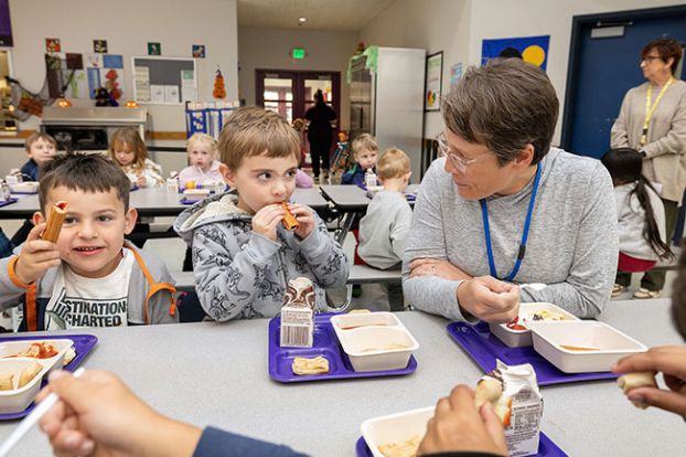 Rachel Thompson/News-Register##McMinnville School Board member Christine Bader chats with kindergartner Ender Libasy, center, about his first-ever churro during lunch Tuesday at Willamette Elementary School. At left is his classmate Anthony Leon. Bader visited as part of a districtwide effort to celebrate National School Lunch Week and recognize the vital work of cafeteria staff who feed students each day.