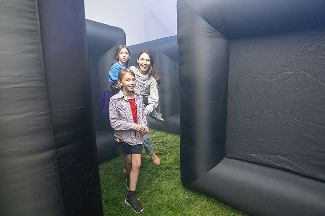 Rachel Thompson/News-Register##Vanessa Holfort carries her daughter Jillian, 8, through Linfield University’s haunted maze as twin sister Genevieve leads the way during Saturday’s Wildcat Harvest Haunt. Families could request a “less scary” version of the maze before entering. Hosted by ASLU, Linfield’s student government organization, the event featured carnival games, food trucks, a petting zoo, and both spooky and kid-friendly thrills. Formerly just for Linfield students, this year marked its debut as a community event. Rachel Thompson/News-Register##Vanessa Holfort carries her daughter Jillian, 8, through Linfield University’s haunted maze as twin sister Genevieve leads the way during Saturday’s Wildcat Harvest Haunt. Families could request a “less scary” version of the maze before entering. Hosted by ASLU, Linfield’s student government organization, the event featured carnival games, food trucks, a petting zoo, and both spooky and kid-friendly thrills. Formerly just for Linfield students, this year marked its debut as a community event.
