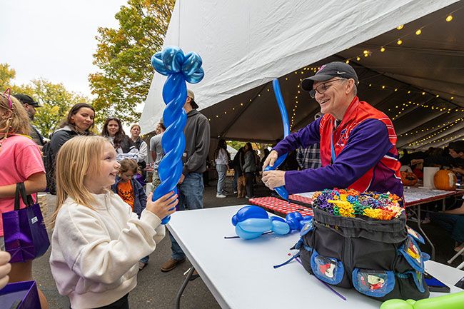 Rachel Thompson/News-Register##Zoe Cook, 7, watches as Linfield wrestling coach Frank Johnson twists a balloon whale. Johnson, who coaches both the men’s and women’s teams, delighted kids with balloon creations at the event tent. Rachel Thompson/News-Register##Zoe Cook, 7, watches as Linfield wrestling coach Frank Johnson twists a balloon whale. Johnson, who coaches both the men’s and women’s teams, delighted kids with balloon creations at the event tent.