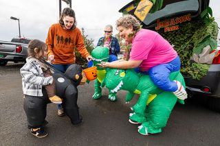 Rachel Thompson/News-Register##Kristianna Groling of McMinnville helps her 4-year-old son Lyric, hitching a ride on a gorilla, collect candy from Lisa Boschee and Patty Williams of the Willamette Valley Cancer Foundation at their Jurassic Park–themed trunk during Lum’s Trunk or Treat on Friday.