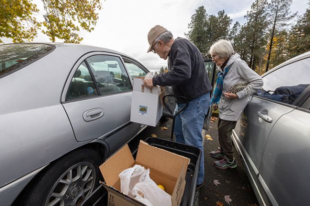 Rachel Thompson/News-Register##Mark Pitts, who led the crew of volunteers in prayer before the food pantry opened Tuesday, lifts boxes of groceries into Sharon Butalla’s car. The McMinnville woman said coming to Hope on the Hill really helps her have enough food.