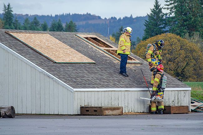 Rachel Thompson/News-Register##Fire Chief Reed Godfrey, left, stands with firefighter Josh Coon, center, and Capt. Kody Quinlan near a roof ventilation training prop during a multi-company exercise Wednesday in McMinnville. The drill simulated vertical ventilation — cutting through the roof to release heat, smoke and gases. “When seconds count, it’s not really the time to learn how to start a chainsaw or climb a roof,” Godfrey said. “That’s why it’s imperative that we get out and do these types of things.”