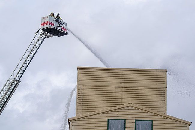 Rachel Thompson/News-Register##Firefighters Kelly Vallance and Jake Perry spray water from an aerial platform during a defensive fire simulation Wednesday morning at the McMinnville Fire District’s drill tower. Crews transition to this “big water” operation when a fire is too dangerous to fight from inside, applying up to 2,000 gallons per minute from above.