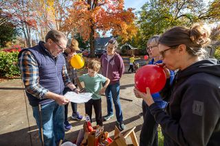 Rachel Thompson/News-Register##Watched closely by Lev Martin, 7, Ham Fam run founder Michael Hampton looks over a checklist of supplies for the Thanksgiving event while neighbors Jennifer Dederich, next to Hampton, and Courtney Martin, right, blow up balloons for the arch that starts and ends the event, Also pictured are Liz Wilkins, center, one of the neighbors who are continuing the Thanksgiving morning tradition, and Laura Hampton, who cofounded the event and ran it with her family for 13 years.