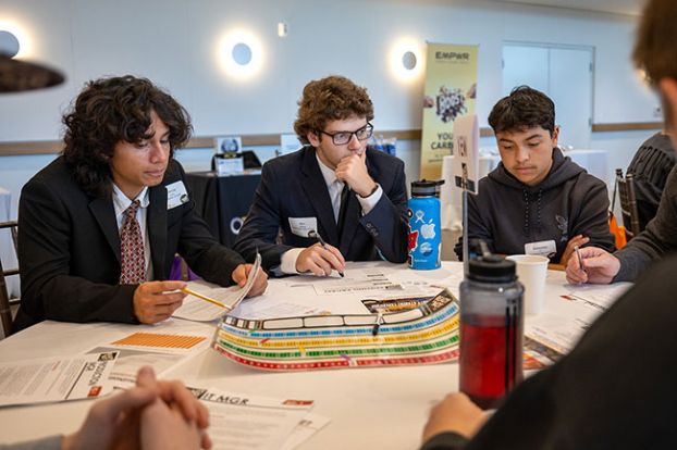 Rachel Thompson/News-Register##Ben Mackay of McMinnville High School, center, Chenoa Lopez of the Delphian School, left, and other students discuss the best way to handle a sudden crisis in their stand-up paddleboard manufacturing company. They confronted situations such as the loss of a key piece of equipment, new taxes and a recession.