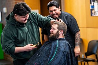 Rusty Rae/News-Register##Barber Jose Mojica (left) asks Mac PD officer Derek Randall if he’s ready for a new look, as barber John Brooks laughs. “I haven’t seen my face in probably seven years,” Randall said. The results are pictured below.